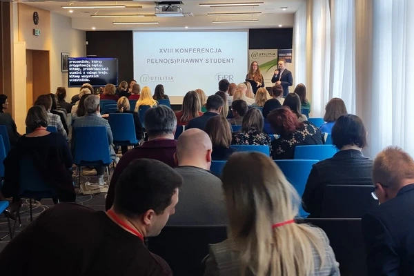 Zdjęcie z konferencji Pełno(s)prawny Student. Na zdjęciu widać siedzących uczestników szkolenia i prelegentów. Prezentację, ekran z wyświetlanym na żywo tekstem, rollupy współorganizatorów.